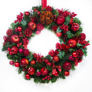 A green wreath is decorated with red apples, bells, berries, balls and pine cones.