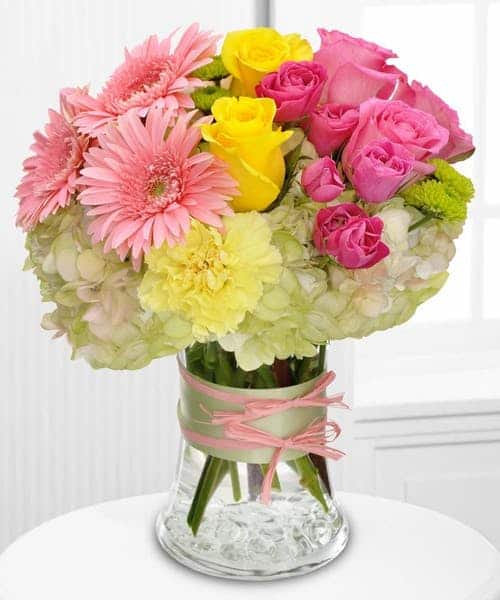 Send a glamorous floral gift to the style maven in your life, including roses, gerberas and hydrangea, in delicate hues of pink, yellow and green – all dressed up with ribbon and raffia. Approximately 10" (W) x 11" (H)