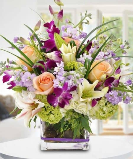Purple dendrobium orchids are set in contrast with peach roses and green hydrangea