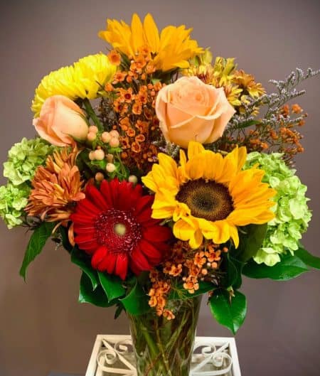 This tall vase includes the seasons finest. Bright sunflowers, green hydrangea, roses, gerbera daisies, berries and wax flowers are all arranged in this seasonal stunner.